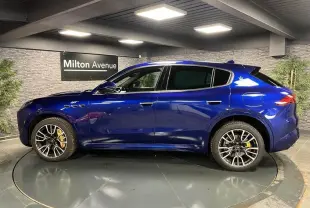 Profil droit du Maserati Grecale bleu avec jantes noires et étriers de freins jaunes visibles en intérieur showroom.