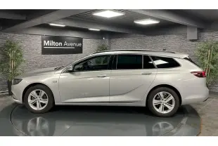 Opel Insignia Sports Tourer gris métallisé vue de profil côté gauche dans un showroom avec mur en pierre.