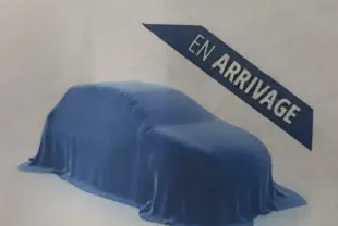 Vue 3/4 avant d'une Dacia Sandero 2026 gris schiste, couverte d'une housse bleue avec un panneau "Entretien" en arrière-plan.