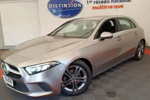 Vue 3/4 avant d'une Mercedes Classe A 180 Business Line gris clair avec jantes alliage et phares LED allumés.