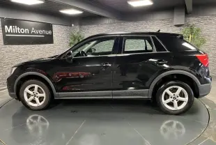Profil côté gauche d'un Audi Q2 noir brillant 2022 avec jantes aluminium 16 pouces dans un showroom intérieur.
