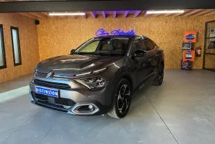 Vue 3/4 avant droite d'une Citroën C4 X gris métallisé 2024 avec phares LED et jantes noires en intérieur showroom.
