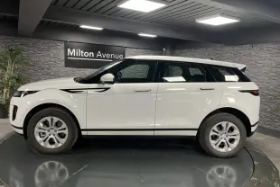 Range Rover Evoque blanc vu de profil côté gauche dans un showroom avec murs en pierre grise.