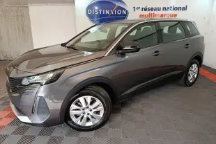 Peugeot 5008 gris clair vue 3/4 avant droit, avec jantes alliage et feux LED dans un showroom intérieur.