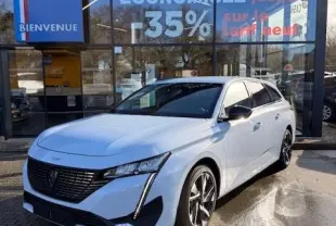 Peugeot 308 Hybrid blanc vue 3/4 avant droit, avec calandre noire et feux LED distinctifs, devant un showroom.
