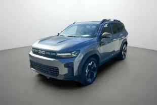 Dacia Bigster gris schiste en 3/4 avant droit avec jantes alu noires et barres de toit visibles.