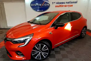 Vue 3/4 avant droite d'une Renault Clio Initiale Paris orange vif dans un showroom avec sol damier noir et rouge.