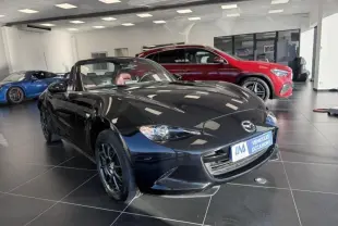 Mazda MX-5 noir 2020 en 3/4 avant droit, capote ouverte, intérieur rouge visible dans un showroom lumineux.