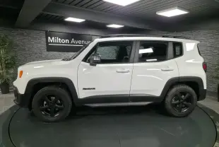 Profil côté gauche d'un Jeep Renegade blanc 2018 avec jantes noires 5 branches et barres de toit gris clair.
